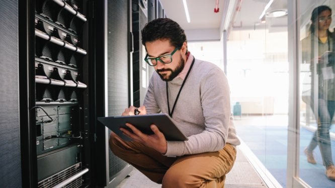 IT professional kneeling in from of server racks, analyzing diagnostics